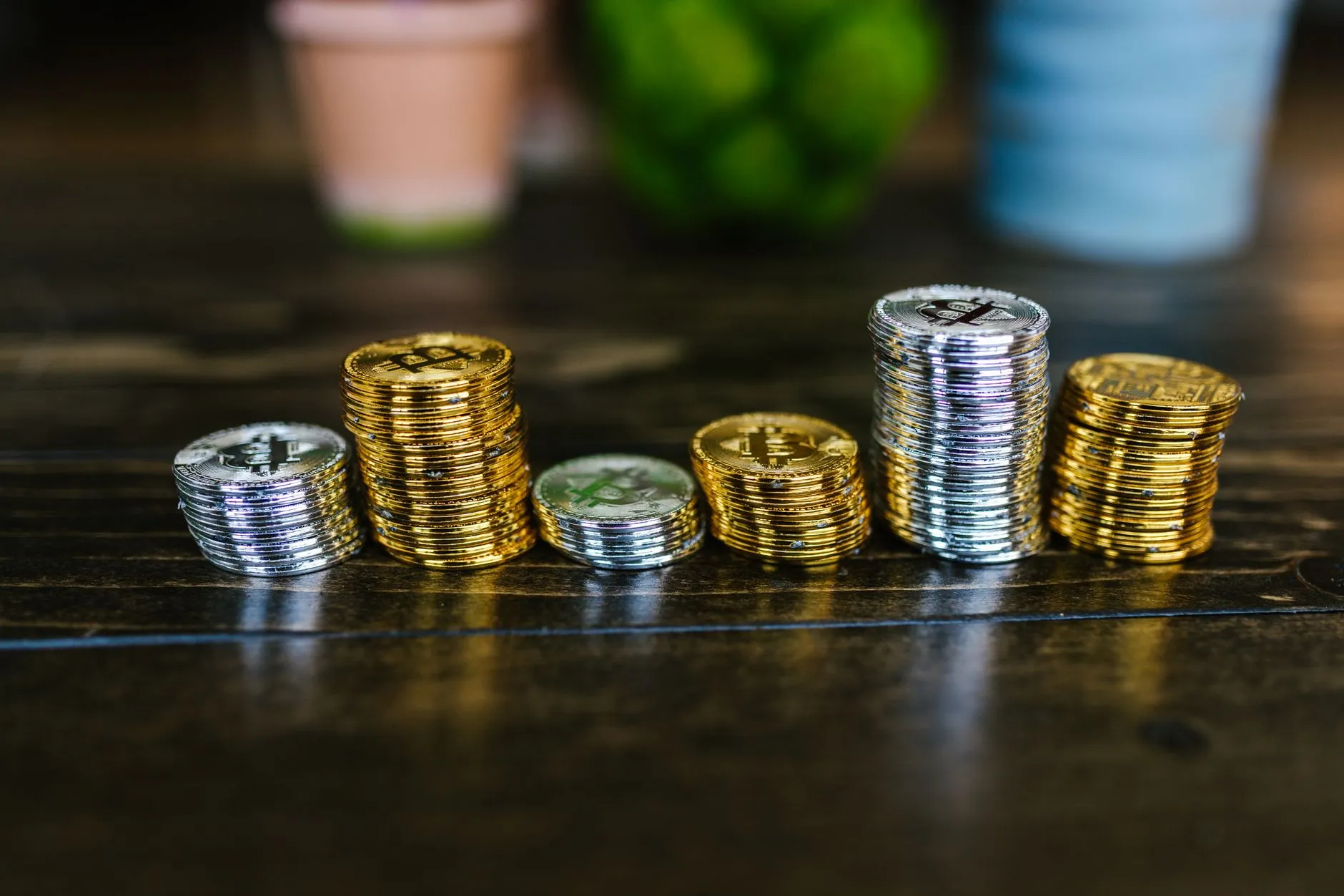 Ascending stacks of gold and silver crypto coins on a dark wooden desk, illustrating staking rewards accruing over time
